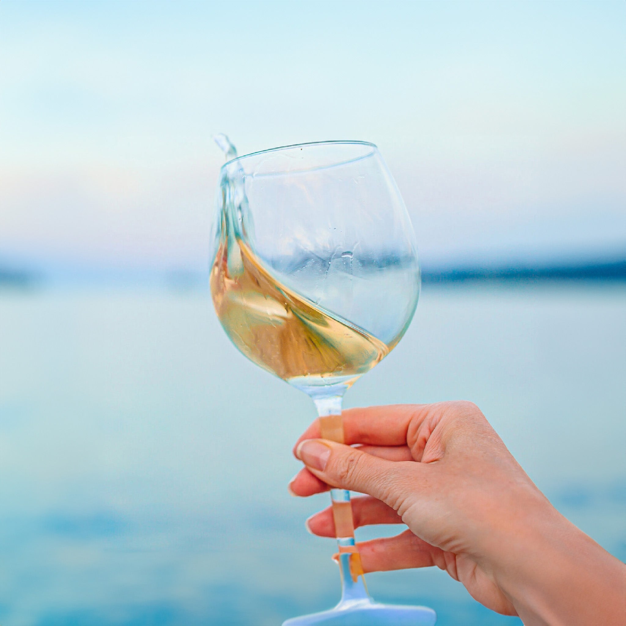 A hand holding a glass of cold white wine with the sea in the background.