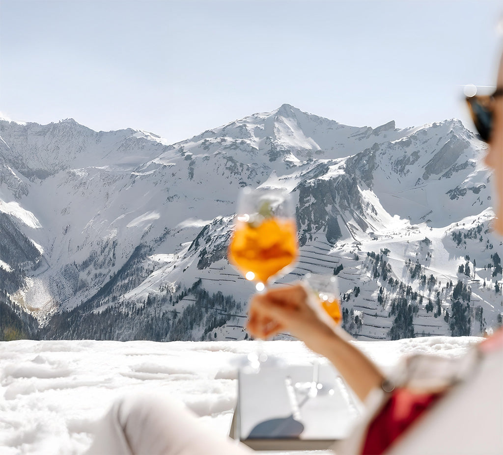 A person holding a glass of coctail against a snowy mountain landscape