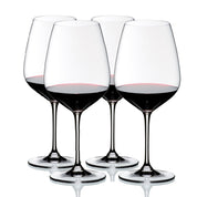 A set of four clear crystal wine glasses with a diamond-shaped bowl, long stems, and circular bases, filled with red wine.