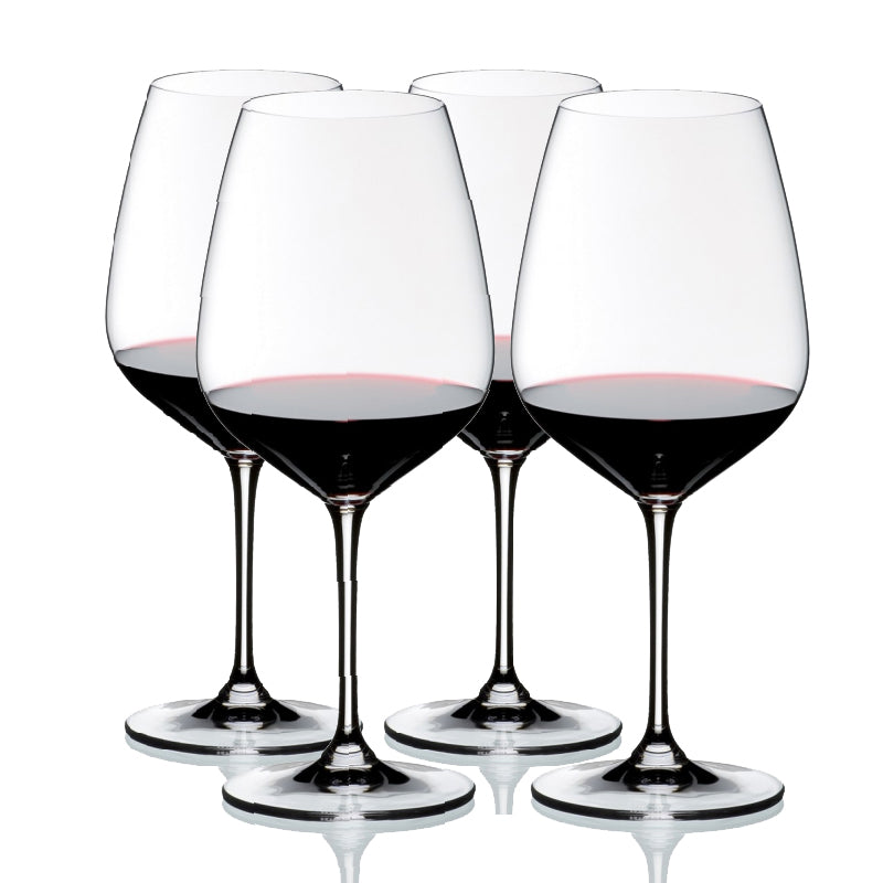 A set of four clear crystal wine glasses with a diamond-shaped bowl, long stems, and circular bases, filled with red wine.