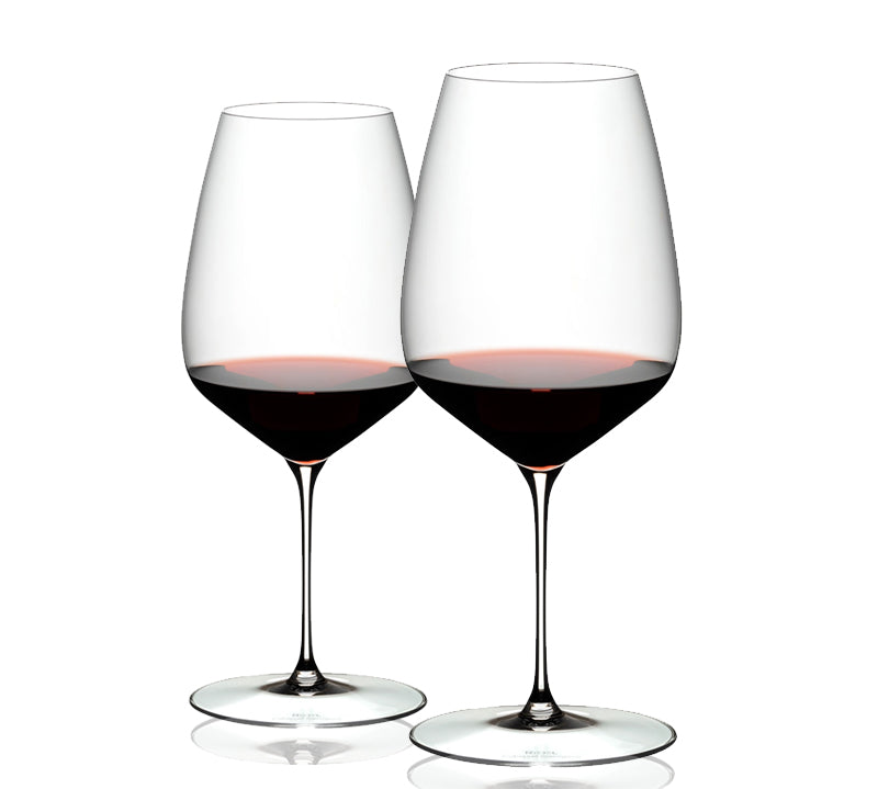 A set of two clear RIEDEL Veloce Cabernet Sauvignon wine glasses filled with red wine, showcasing their slender stems and rounded bowls.