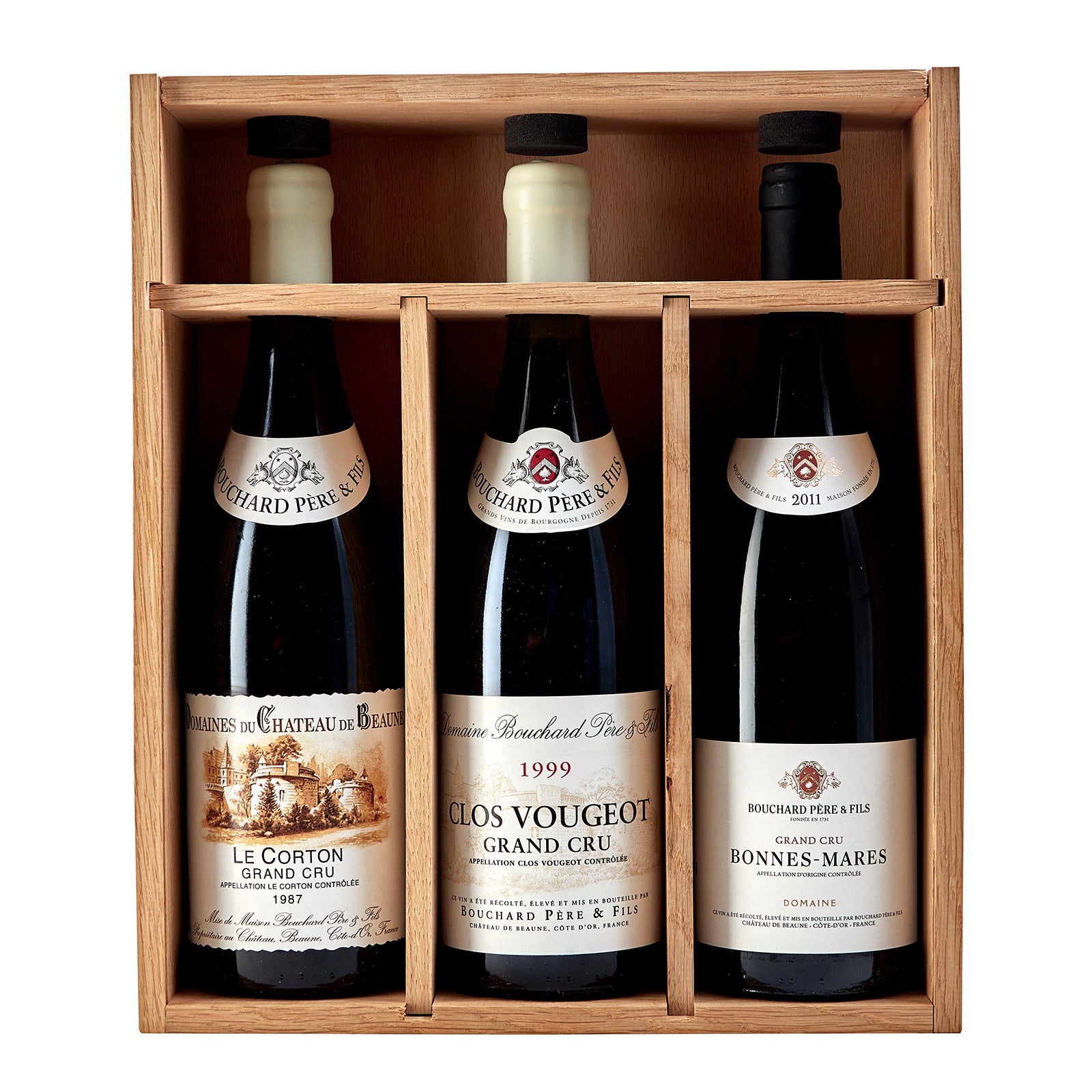 A collector's case containing three bottles of Bouchard Pere & Fils wine, with labels indicating the vintage years 1987, 1999, and 2011, placed in front of a wooden background.