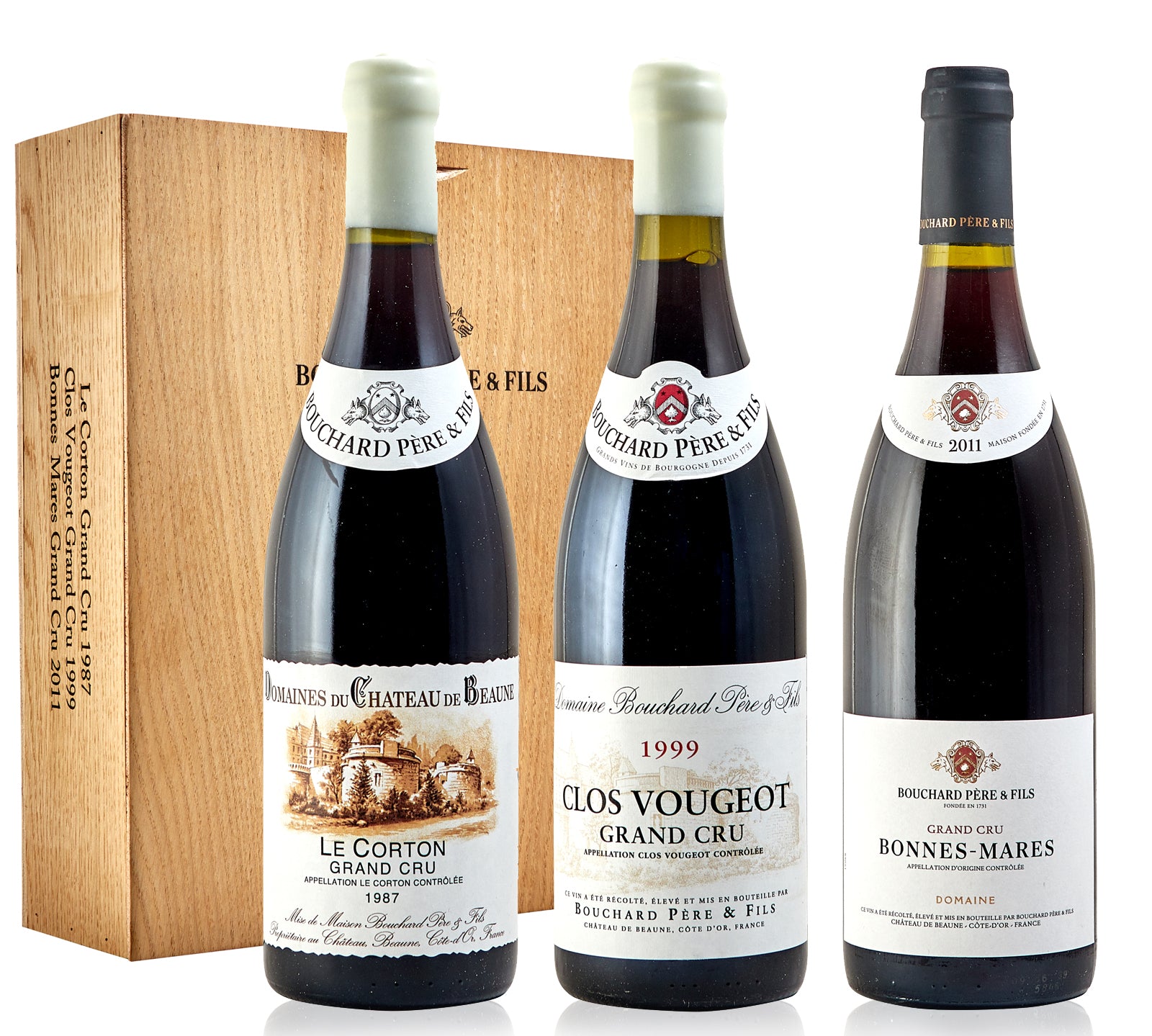 A collector's case containing three bottles of Bouchard Pere & Fils wine, with labels indicating the vintage years 1987, 1999, and 2011, placed in front of a wooden background.